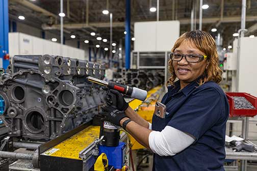 Woman holding a tool next to an engine