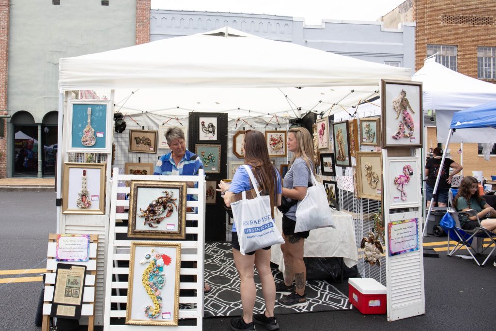 Prairie Arts Festival photo of two women inspecting artwork in a booth